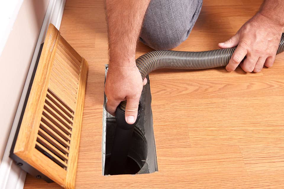 Close-up of a technician performing air duct cleaning service with a vacuum hose